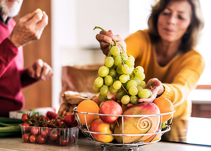Woman holding green grapes from a fruit basket containing apples, oranges, and tomatoes highlighting interesting scientific facts.