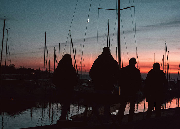 Silhouettes of four people by a marina at sunset with eerie colors and a crescent moon in the sky, scientific facts theme.