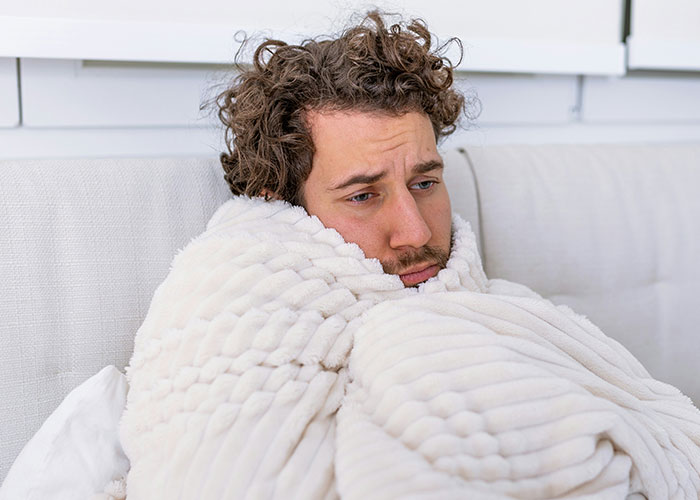 Man wrapped in a soft white blanket looking pensive indoors, illustrating eerie scientific facts about human behavior.