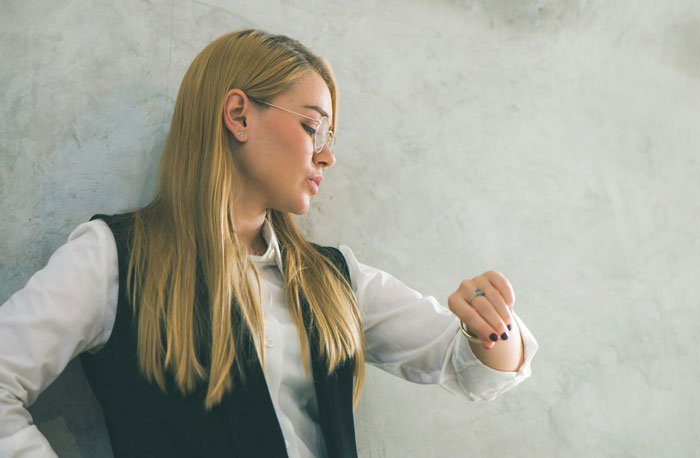 Young live-in nanny in a vest and glasses looking at her watch, reflecting on curfew set by mom on nights off