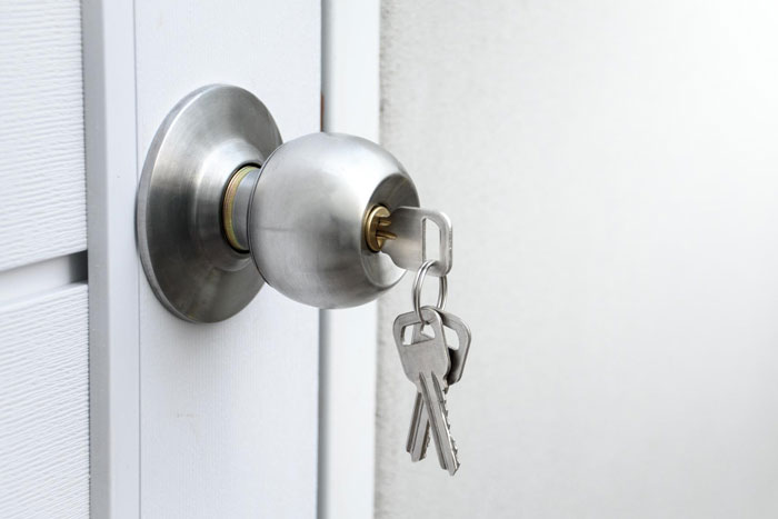 Door lock with keys inserted in a silver doorknob, symbolizing security for a bedroom in a creepy MIL scenario.