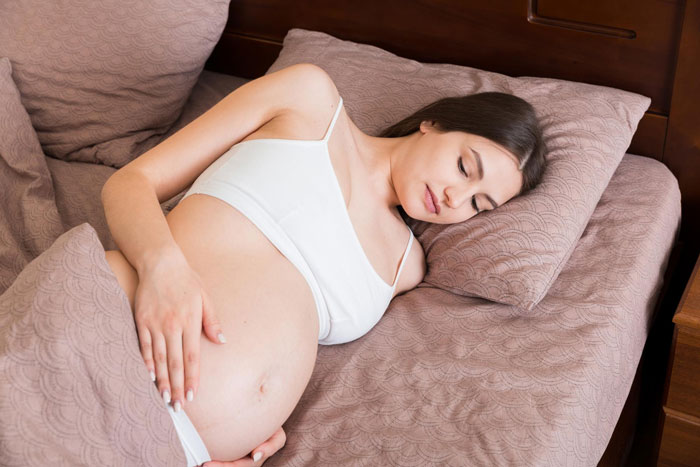 Pregnant woman sleeping on bed with hand on belly, illustrating concerns about creepy MIL watching and privacy issues.