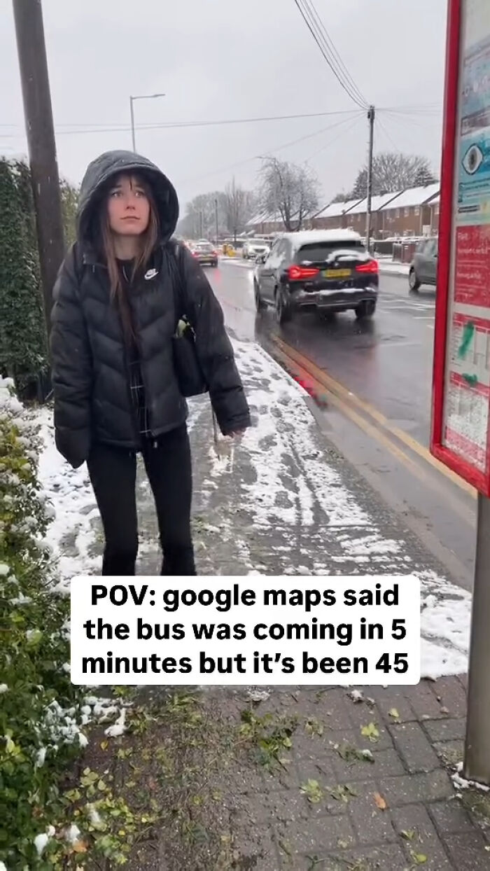 Young woman in a black jacket waits at a snowy bus stop, capturing a great London meme about bus delays and UK humor.