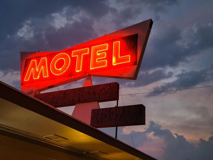 Red neon motel sign glowing at dusk under a cloudy sky, illustrating Americans finding a loophole and using it.