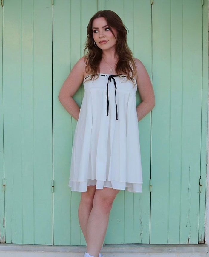 Young woman in a white dress posing against a mint green wooden door, related to Richard Gere&rsquo;s multimillion-dollar home news.