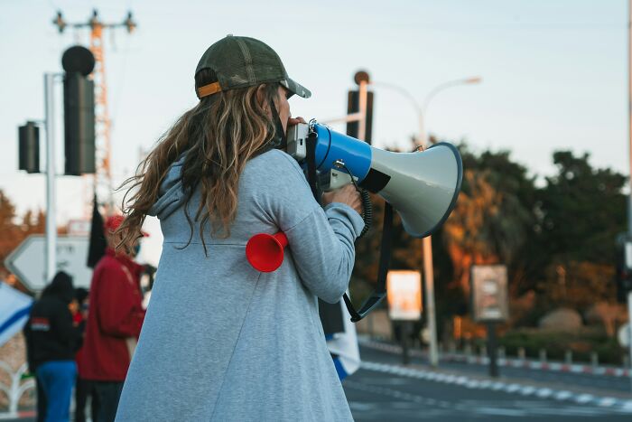 Person wearing a cap and gray hoodie using a megaphone outdoors, symbolizing bold decisions with massive impact on the world.