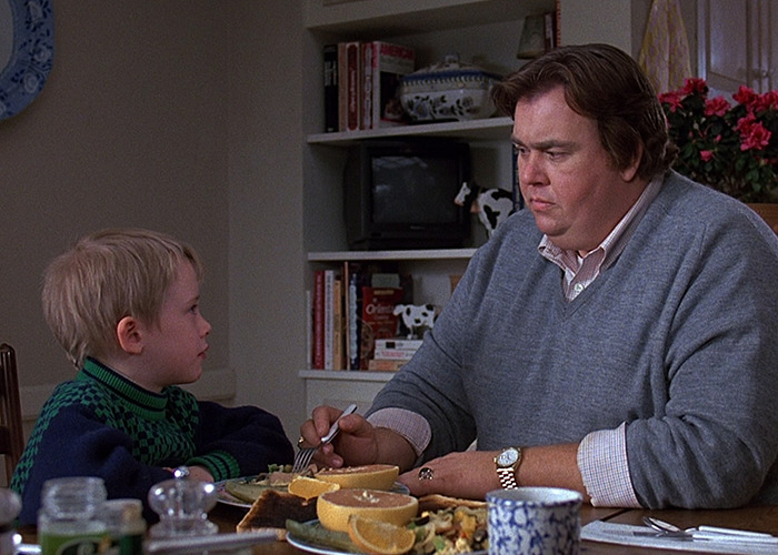 Macaulay Culkin and John Candy share a serious moment at a dining table in a home setting. Macaulay Culkin and John Candy share a serious moment at a dining table in a home setting.