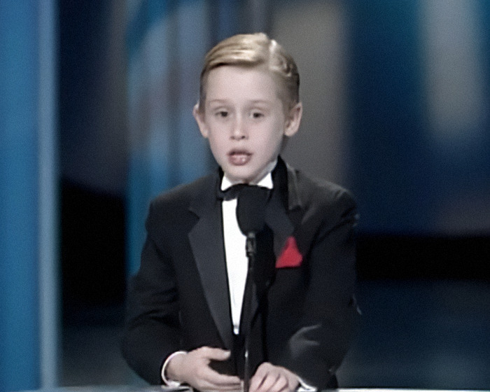 Macaulay Culkin as a child, dressed in a tuxedo, speaking at a microphone during an award event. Macaulay Culkin as a child, dressed in a tuxedo, speaking at a microphone during an award event.