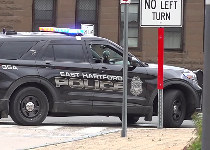 East Hartford police SUV with flashing lights parked near no left turn sign at street intersection.