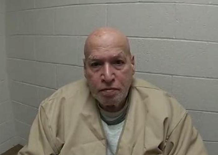Mugshot of a man in a beige prison uniform against a gray cinder block wall, related to brutal cold case police investigation.