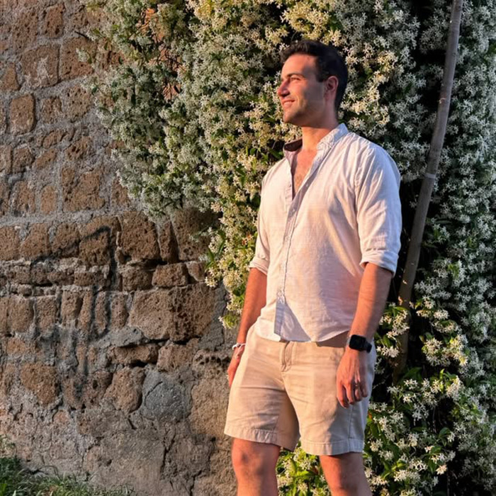 Man standing outdoors near stone wall and flowers, relating to Charlie Kirk bullying claims in high school.
