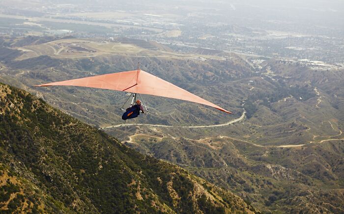 Person hang gliding over mountainous terrain with expansive valley views, illustrating unusual ways people died scenarios.
