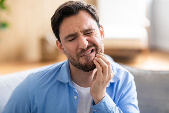 Man in blue shirt sitting on a couch, showing pain and discomfort, symbolizing doctors and nurses haunting experiences.