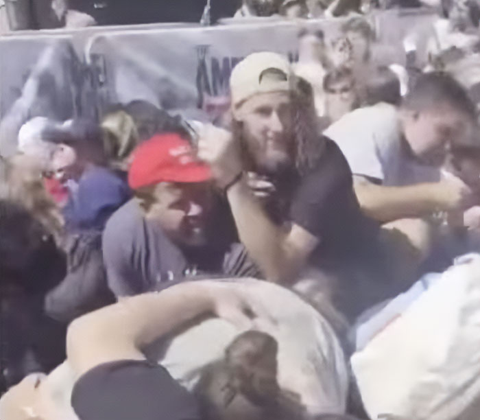 Bearded man in crowd cheering and looking back during chaotic moment at Charlie Kirk event.