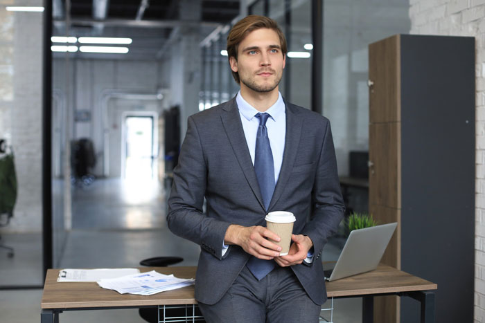 Young professional male dressed formally holding coffee cup in modern office, illustrating strict dress code compliance. Young professional male dressed formally holding coffee cup in modern office, illustrating strict dress code compliance.