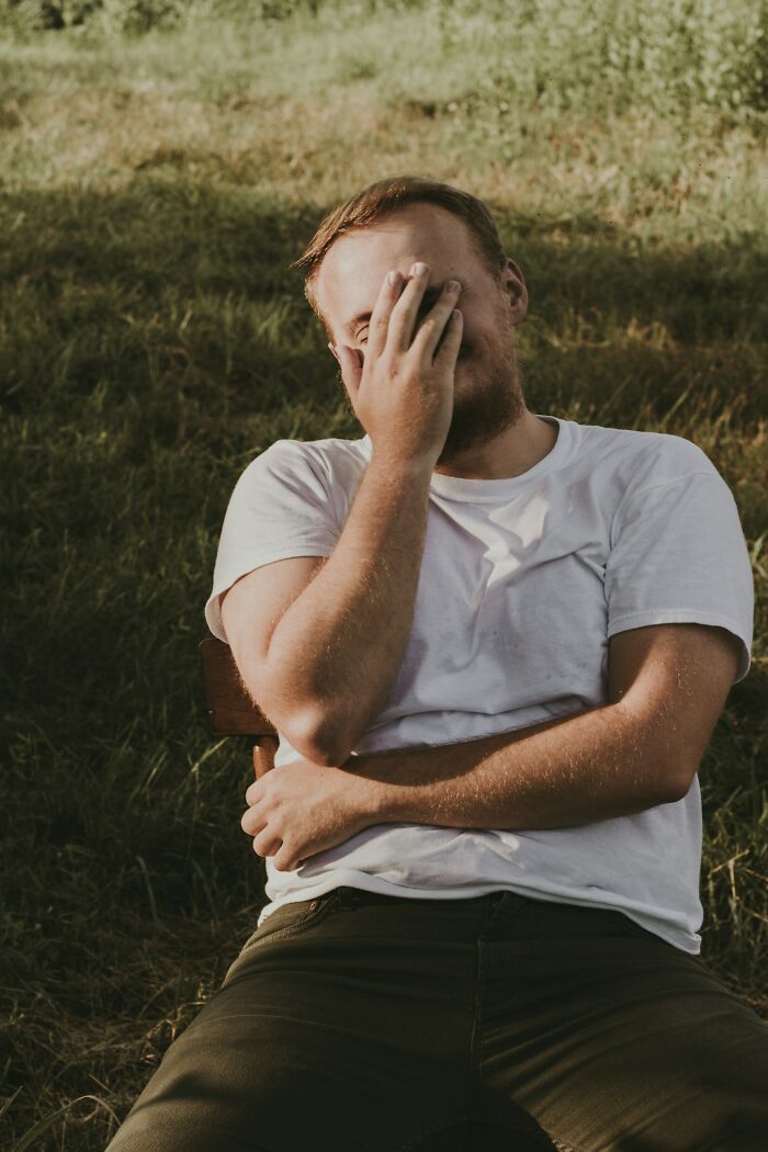 Man sitting outdoors covering his face with one hand, reflecting the challenges of being a tattoo artist with difficult clients.