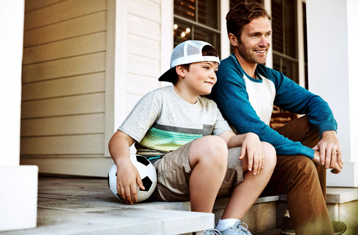 Man and stepchild sitting on porch steps smiling, holding soccer ball, illustrating marriage kids stepkids relationship.