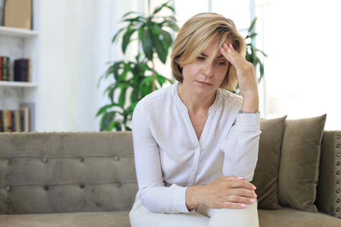Woman appearing stressed and thoughtful while sitting on a couch, reflecting on marriage kids and stepkids relationship challenges.