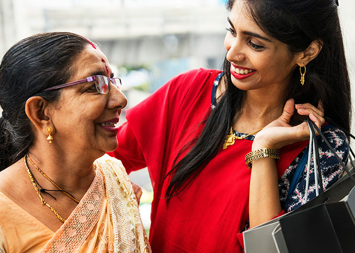 Woman smiling at another woman in traditional attire, hinting at a wedding scene with sister-in-law and bride dynamics.