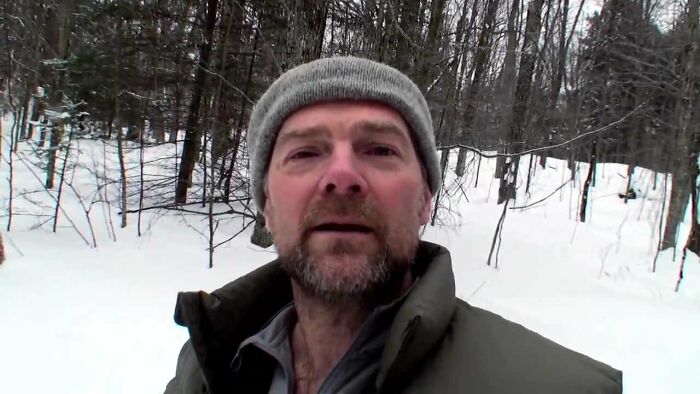 Man wearing a gray beanie and jacket standing outdoors in a snowy forest, representing people running into celebrities and having worst experiences.