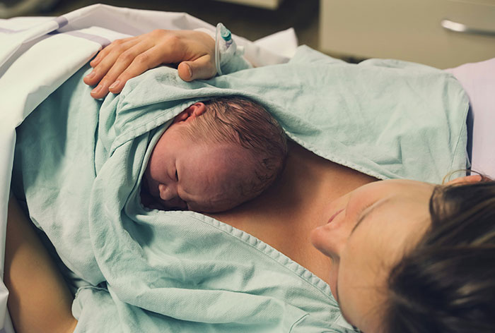 Newborn baby resting on mother's chest in hospital bed, highlighting downplayed medical conditions and procedures.