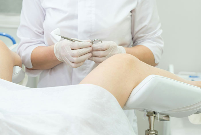Medical professional wearing gloves preparing for a gynecological procedure on a patient in a clinical setting.