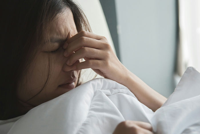 Woman lying in bed with eyes closed, holding nose bridge in pain, illustrating downplayed medical conditions and procedures.