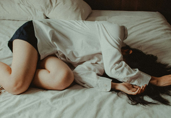 Woman curled up in bed appearing unwell, illustrating the impact of downplayed medical conditions and procedures.