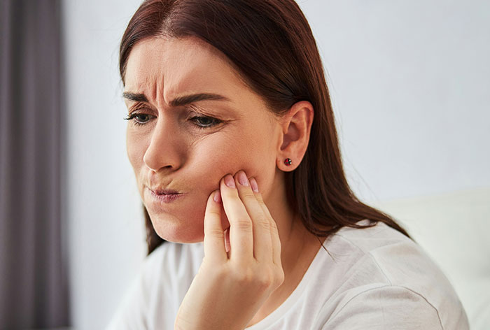 Woman holding her cheek in pain, illustrating downplayed medical conditions and procedures affecting women.