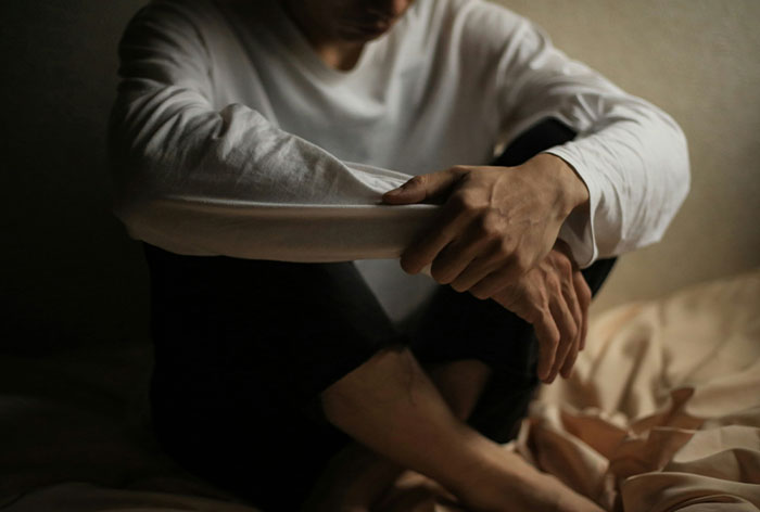 Man sitting alone in dim light, appearing contemplative, illustrating downplayed medical conditions and procedures.