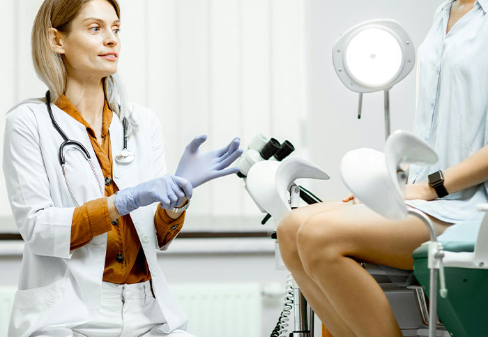 Female doctor wearing gloves during a medical exam with a patient, highlighting downplayed medical conditions and procedures.