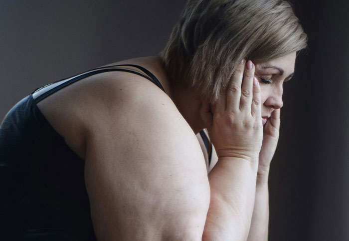 Woman sitting with head in hands, showing strain linked to downplayed medical conditions and procedures affecting women.