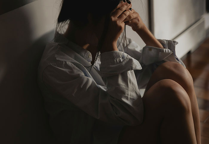 Woman sitting on the floor with hands on her face, illustrating downplayed medical conditions affecting women.