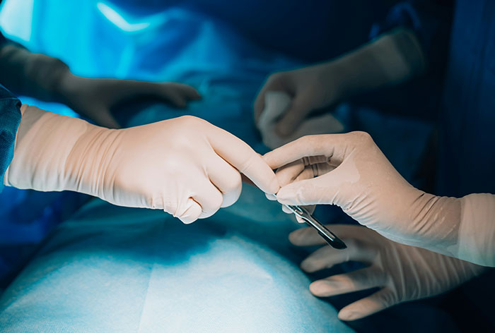 Surgeons wearing gloves performing a precise medical procedure in an operating room with focused lighting.