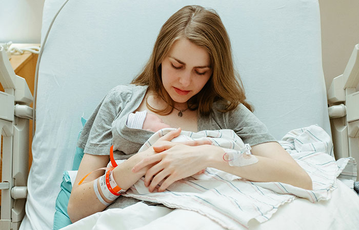 Mother holding newborn baby in hospital bed, highlighting downplayed medical conditions and procedures for women.