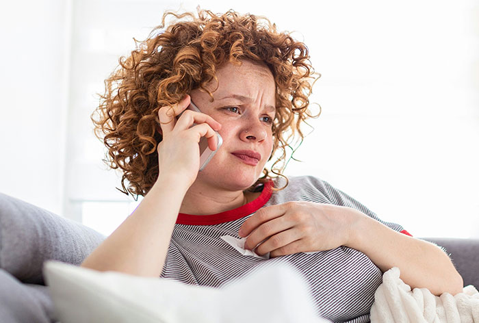 Woman with curly hair looking concerned while talking on phone, illustrating downplayed medical conditions and procedures.