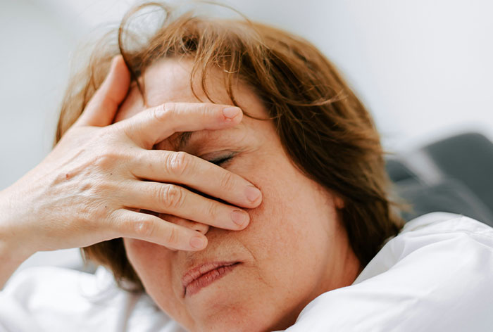 Middle-aged woman holding her face in pain, illustrating downplayed medical conditions and procedures.