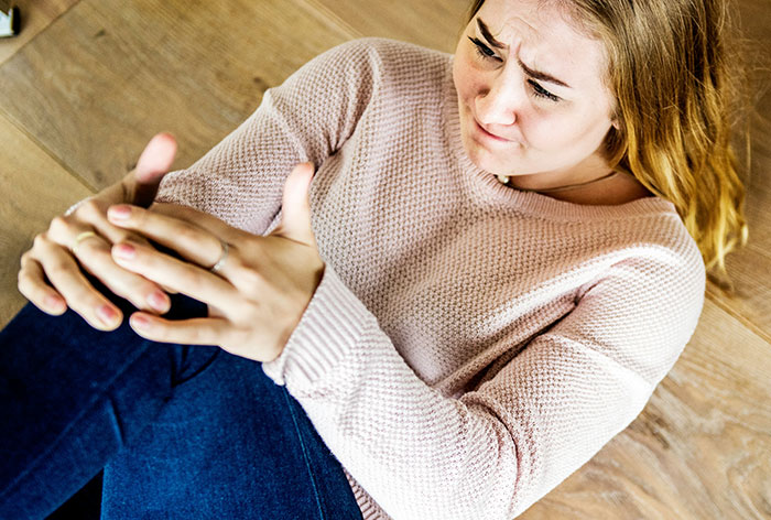 Young woman sitting on floor holding her painful hand, illustrating downplayed medical conditions and procedures.