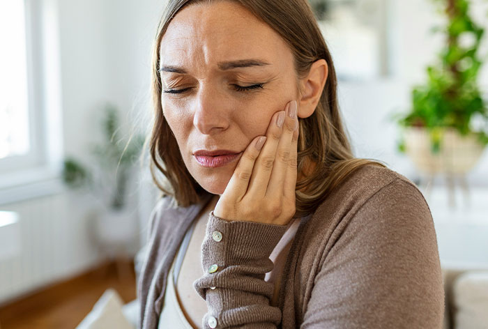 Woman with painful expression holding her cheek, illustrating downplayed medical conditions affecting women.