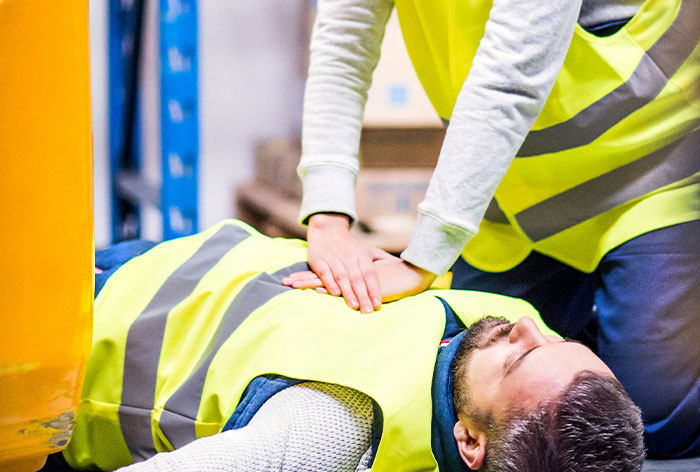Worker performing CPR on a man wearing a safety vest, highlighting downplayed medical conditions and emergency procedures.