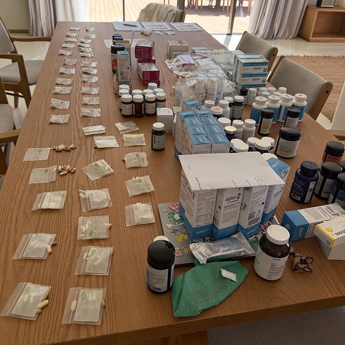 Various medications and supplements organized on a wooden table related to Bella Hadid suffering with darkness and pain.