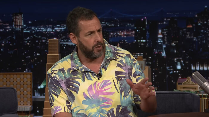 Actor Adam Sandler in a colorful tropical shirt sharing heartwarming celebrity encounters during a late-night talk show.