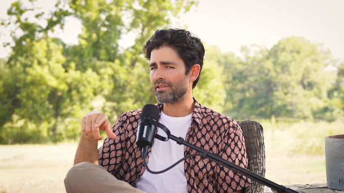 Man in patterned shirt speaking into a microphone outdoors, sharing heartwarming celebrity encounters that still make him smile.