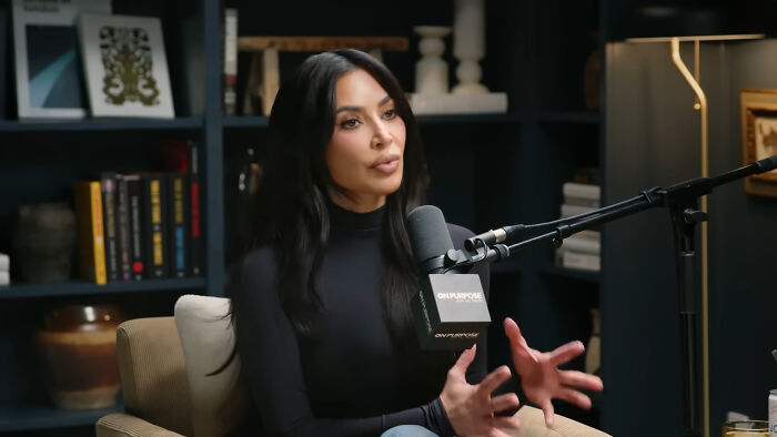 Woman sharing heartwarming celebrity encounters during a recorded interview in a cozy, book-filled studio setting.