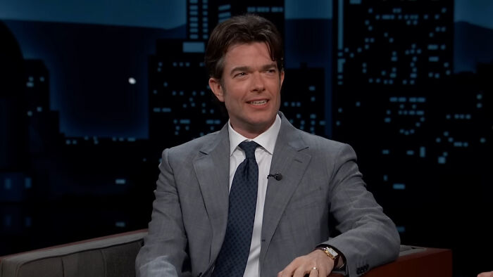 Actor in a gray suit sharing a heartwarming celebrity encounter during a late night talk show interview.