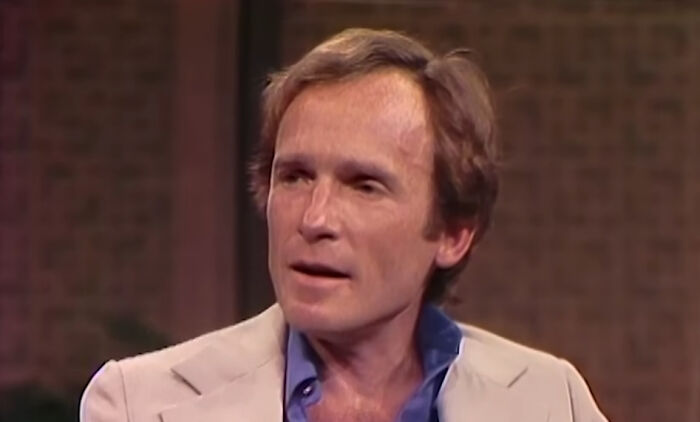 A middle-aged man in a beige blazer and blue shirt sharing heartwarming celebrity encounters in an interview setting.