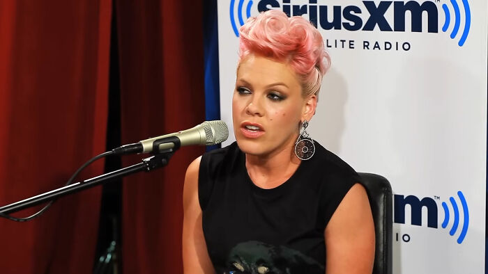 Singer with pink hair speaking into a microphone during a SiriusXM radio interview about heartwarming celebrity encounters.