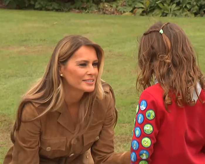 Melania Trump interacting with a young girl outdoors, sparking body double conspiracy after royal family meeting.