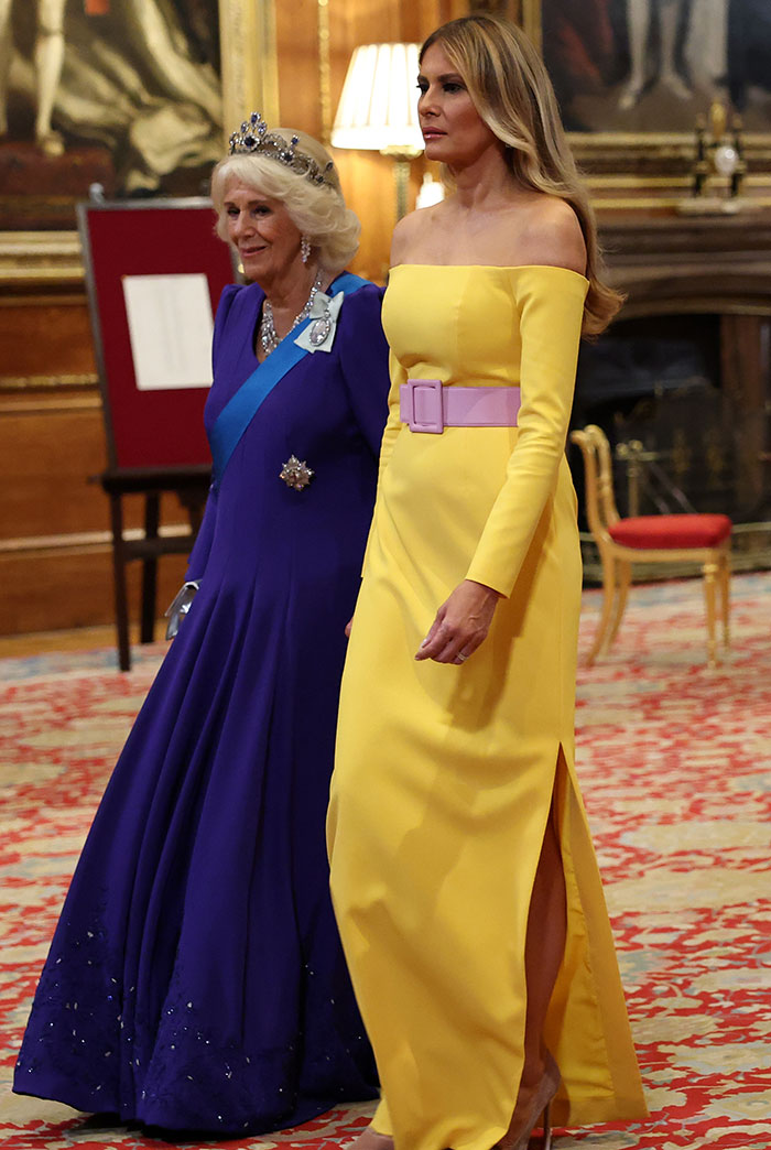Melania Trump wearing a yellow off-shoulder dress with a purple belt, standing beside a woman in a royal blue gown and tiara. Melania Trump wearing a yellow off-shoulder dress with a purple belt, standing beside a woman in a royal blue gown and tiara.