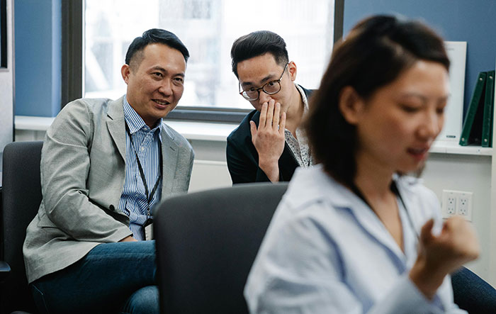 Two male co-workers whisper and make bets about a female colleague in a tense office environment. Two male co-workers whisper and make bets about a female colleague in a tense office environment.